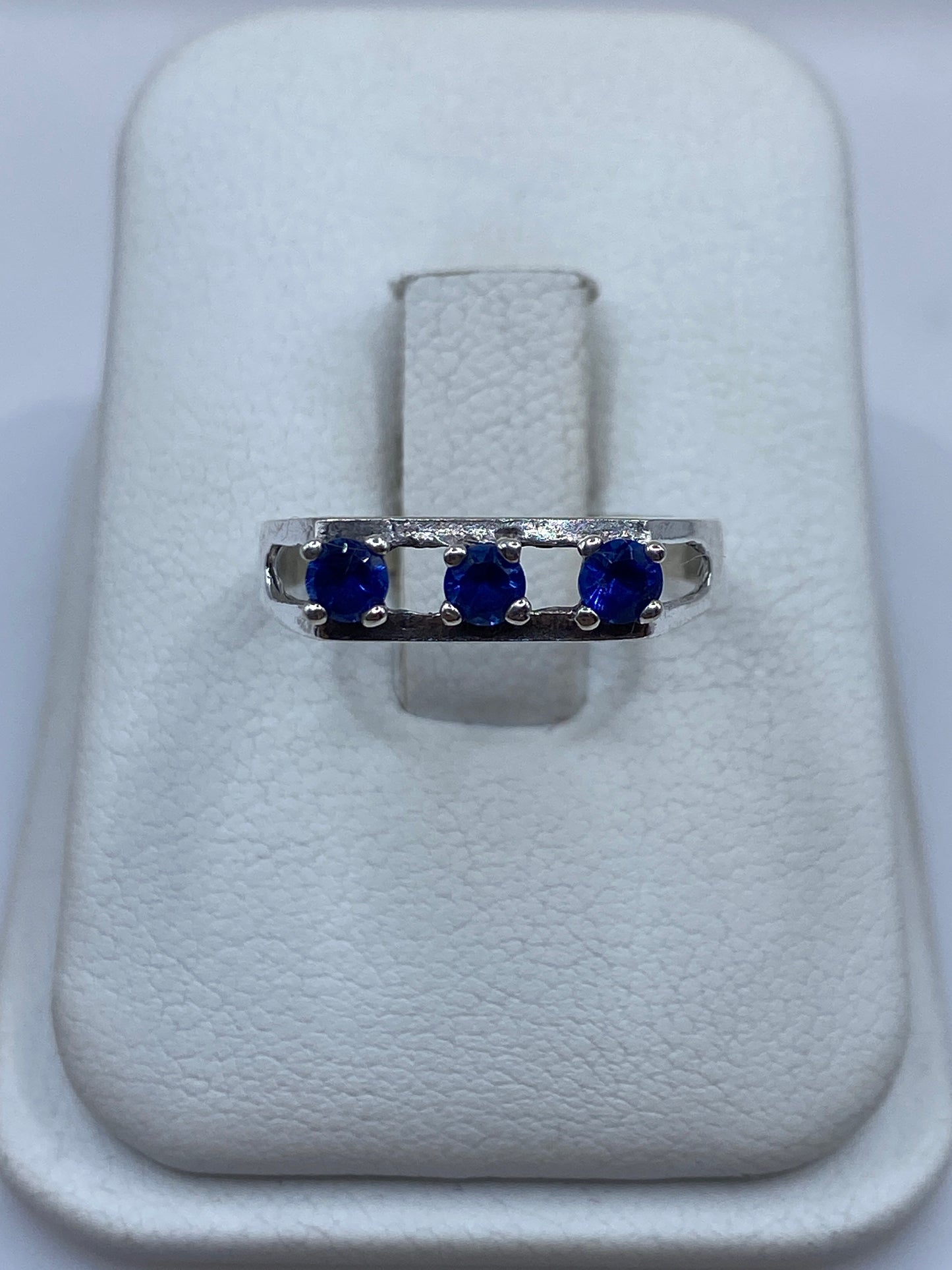 Anillo de plata con tres circonias azules sobre dedo índice, vista frontal minimalista