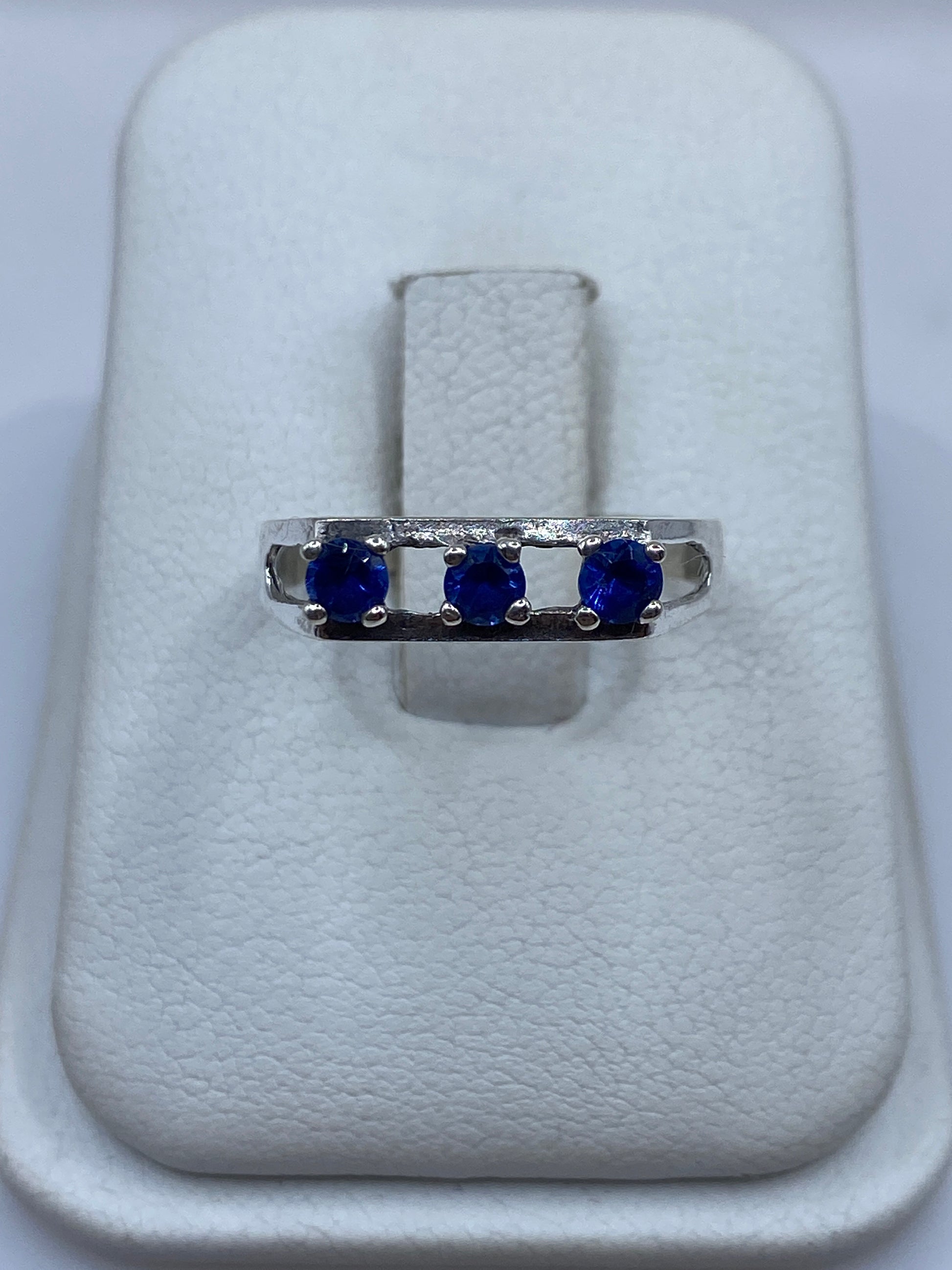 Anillo de plata con tres circonias azules sobre dedo índice, vista frontal minimalista