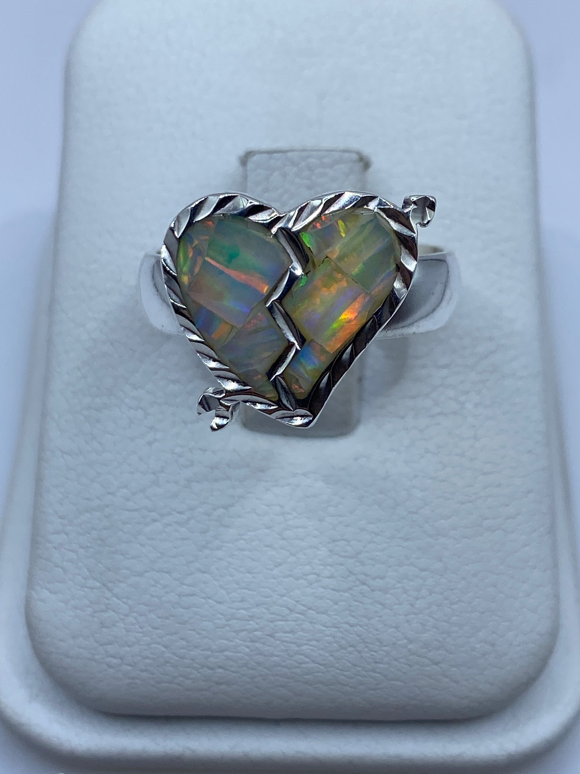 Anillo de plata con ópalo de fuego multicolor exhibiendo destellos naranjas y verdes sobre fondo blanco