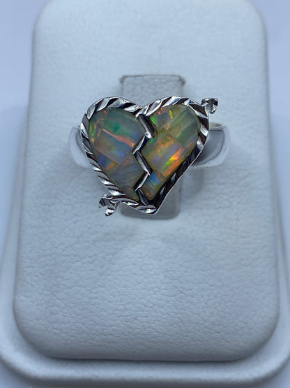 Anillo de plata con ópalo de fuego multicolor exhibiendo destellos naranjas y verdes sobre fondo blanco