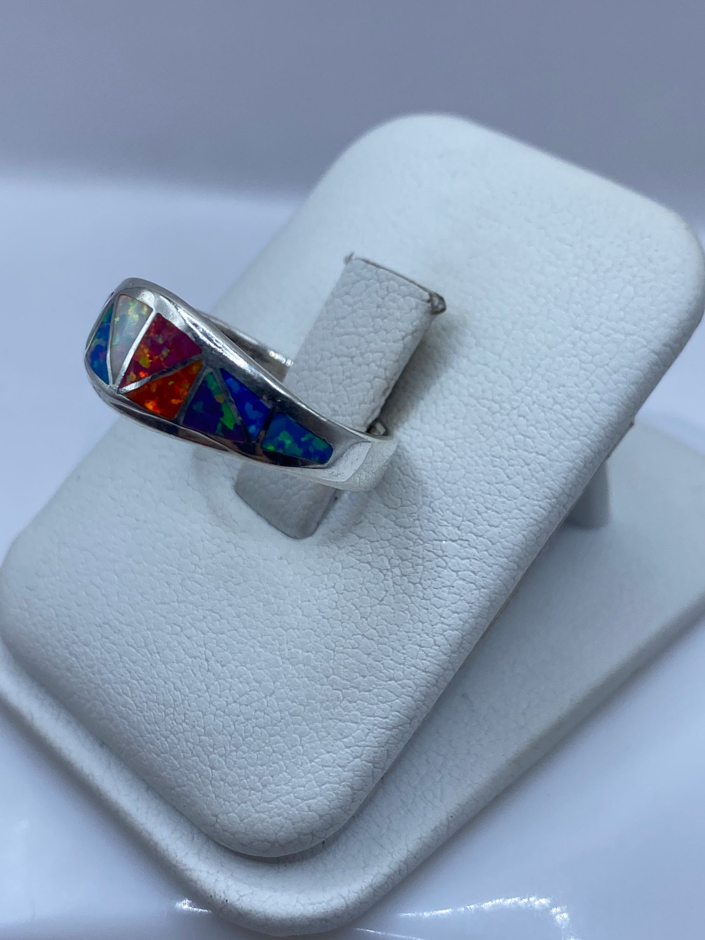 Vista lateral del anillo con ópalo exhibiendo naranja, rojo y azul bajo la luz