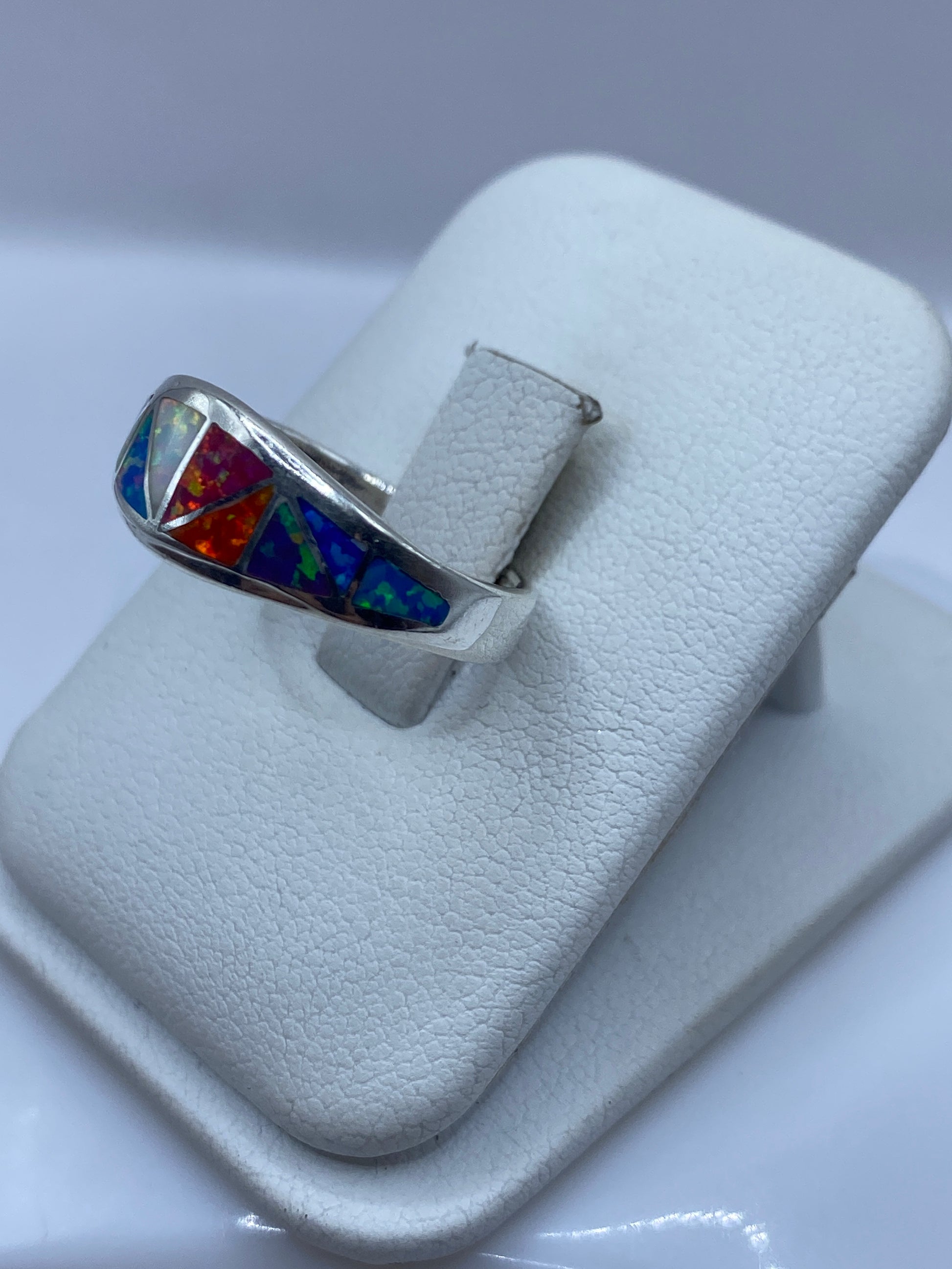 Vista lateral del anillo con ópalo exhibiendo naranja, rojo y azul bajo la luz