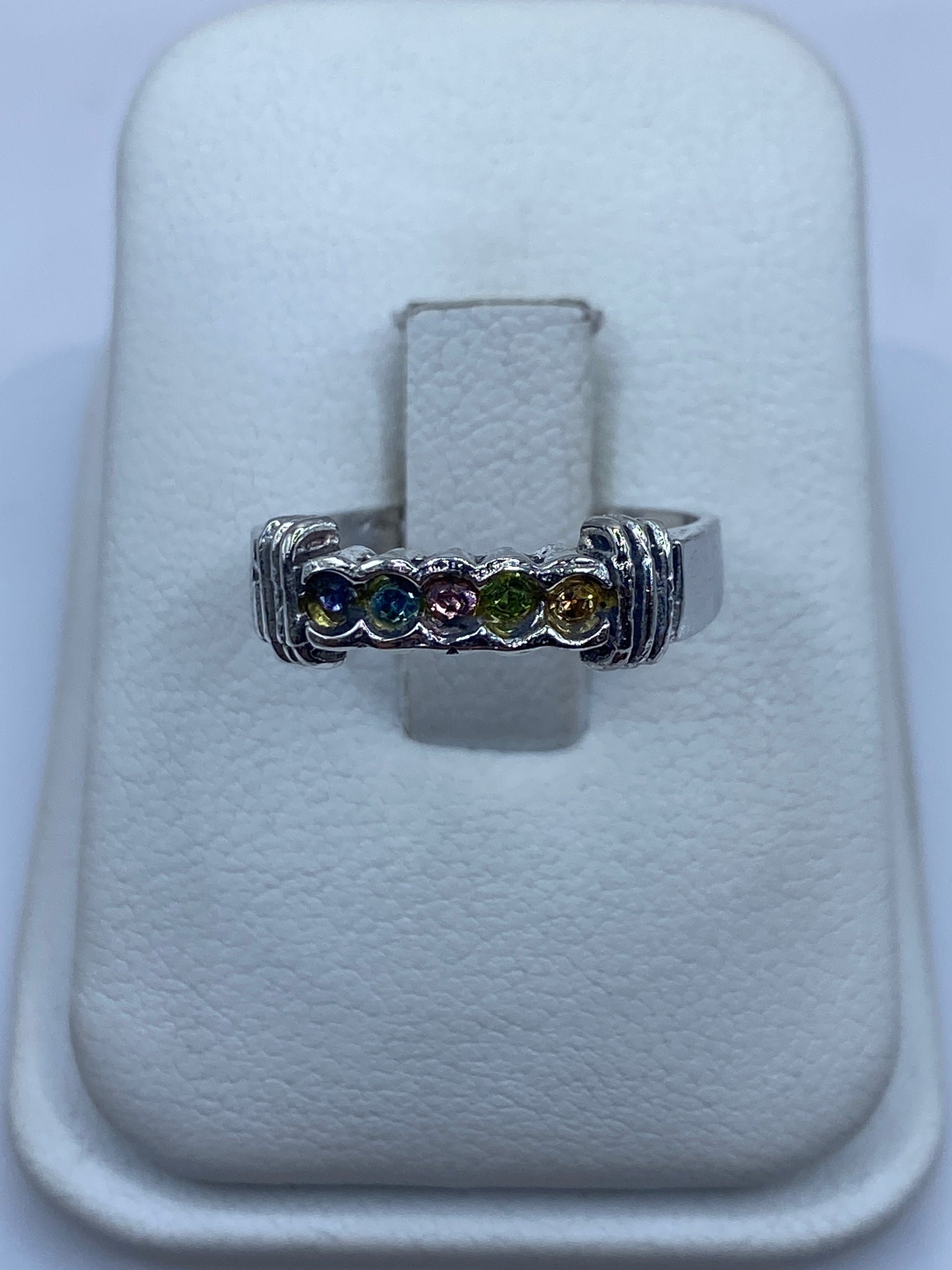 Anillo de plata con circonias multicolor (azul, púrpura, verde, amarillo) sobre presentador blanco