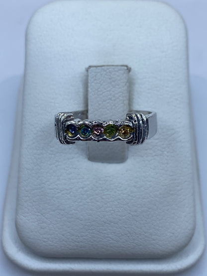Anillo de plata con circonias multicolor (azul, púrpura, verde, amarillo) sobre presentador blanco