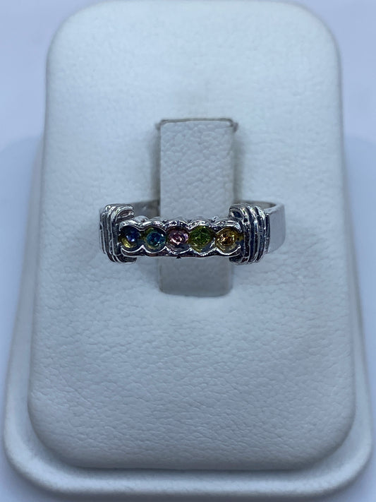 Anillo de plata con circonias multicolor (azul, púrpura, verde, amarillo) sobre presentador blanco