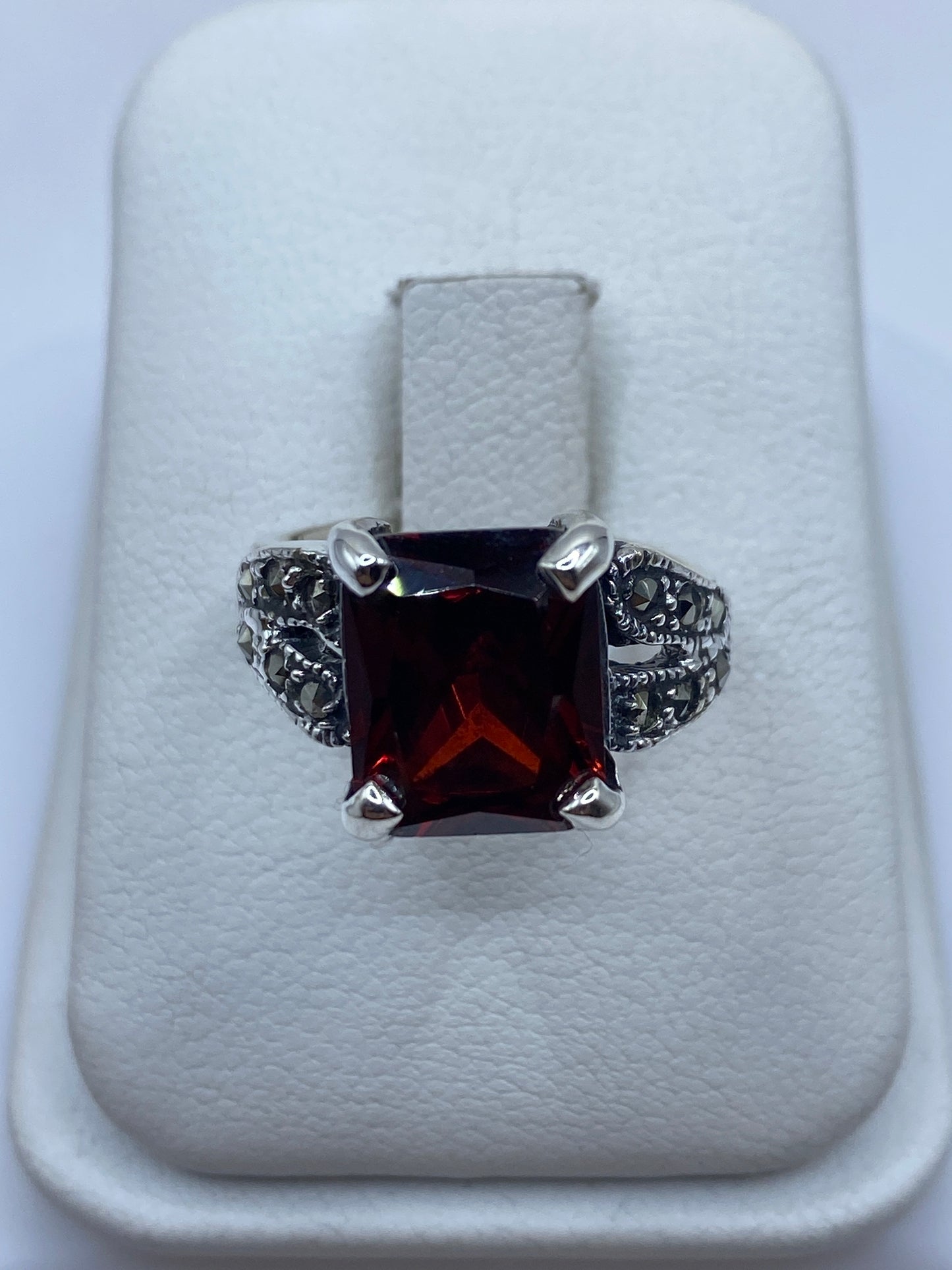 Anillo de plata solitario con circonia roja talla esmeralda, visto de frente sobre cojín blanco