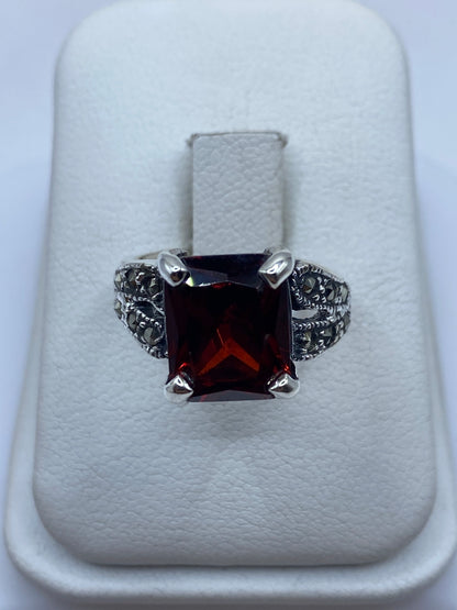 Anillo de plata solitario con circonia roja talla esmeralda, visto de frente sobre cojín blanco