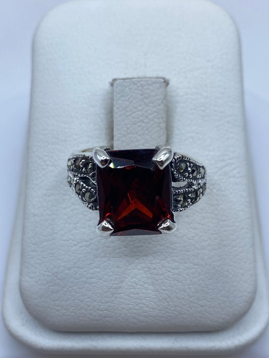 Anillo de plata solitario con circonia roja talla esmeralda, visto de frente sobre cojín blanco