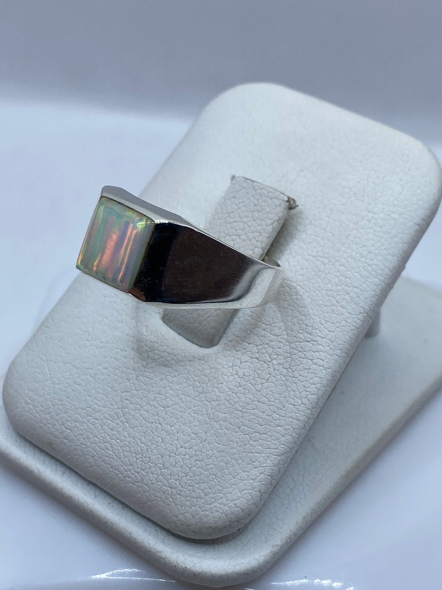 Anillo arquitectónico de plata en dedo con ópalo mostrando juego de colores naranja y verde