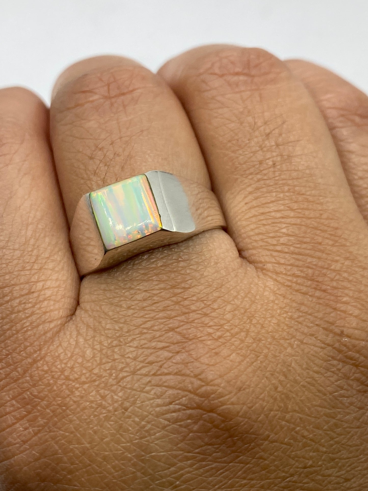 Ópalo de fuego multicolor en anillo de plata .950 sobre fondo gris mostrando variación de colores