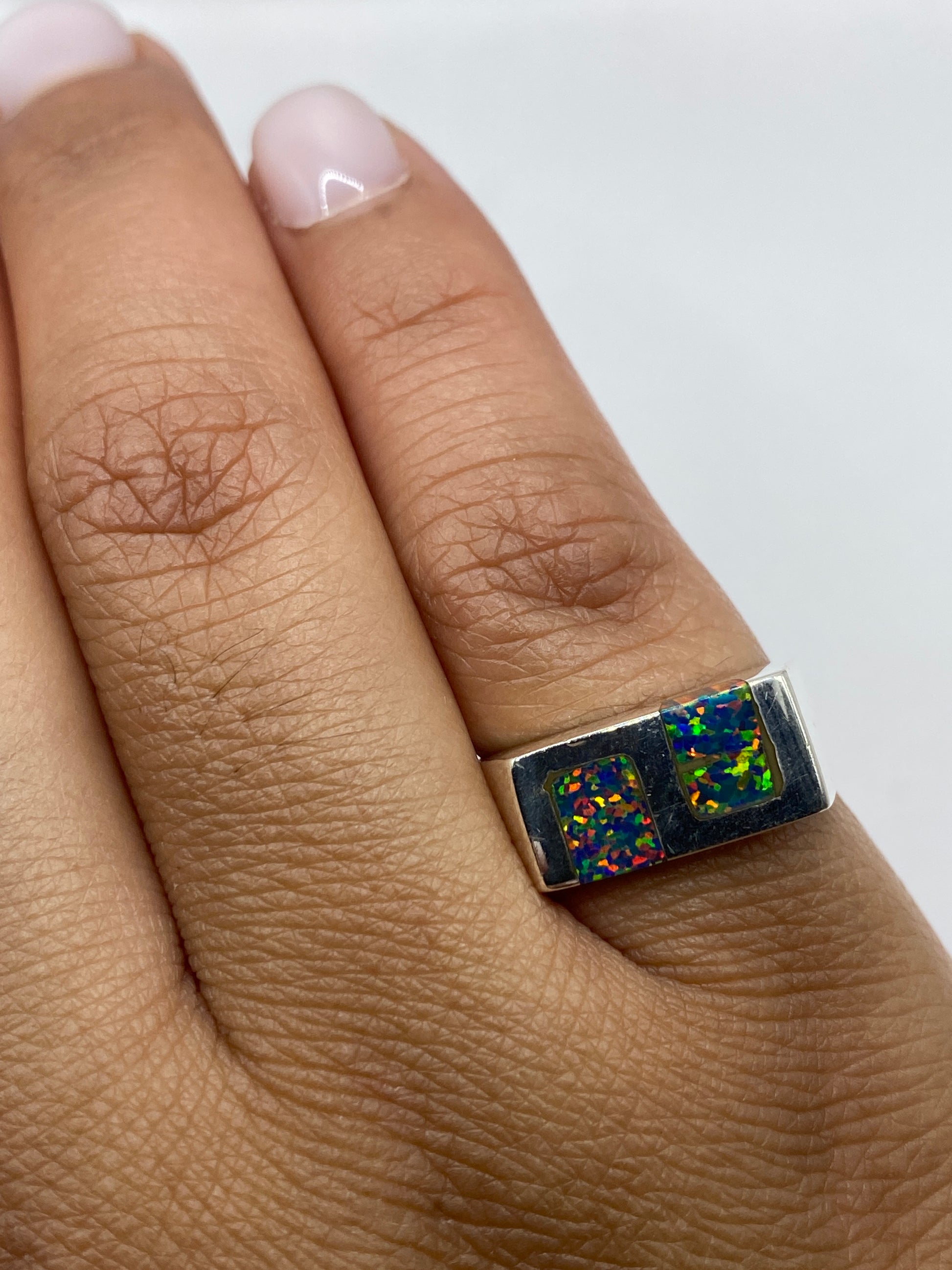 Anillo de plata con ópalo de fuego en dedo, mostrando la paleta multicolor desde ángulo lateral