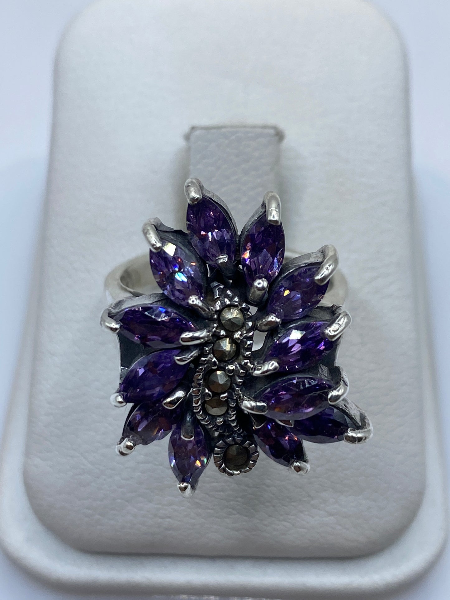 Anillo floral de plata con doce circonias moradas facetadas, diseño voluminoso sobre fondo blanco