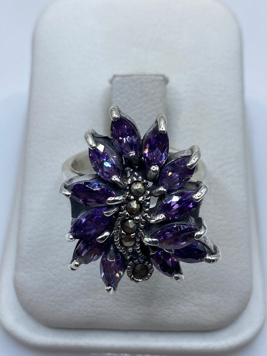 Anillo floral de plata con doce circonias moradas facetadas, diseño voluminoso sobre fondo blanco