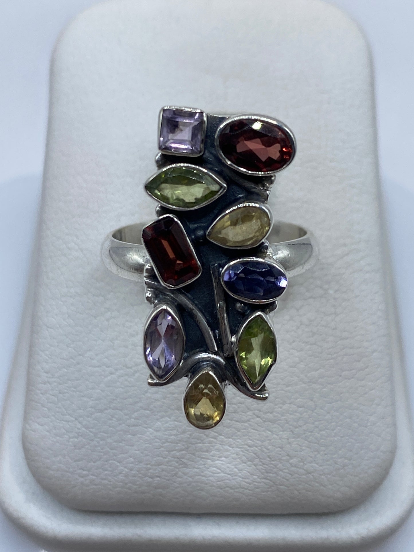 Anillo de plata geométrico con circonias multicolor (morado, ámbar, verde, rojo) en la mano de una mujer
