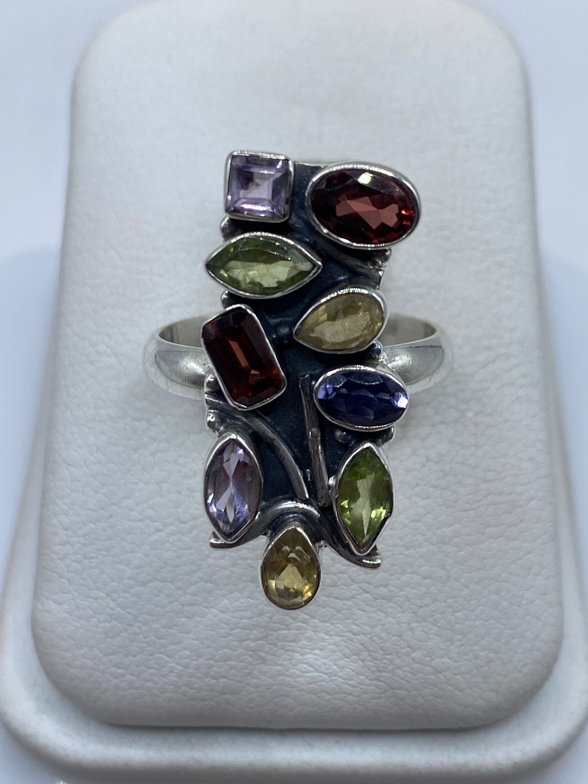 Anillo de plata geométrico con circonias multicolor (morado, ámbar, verde, rojo) en la mano de una mujer