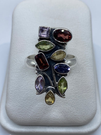 Anillo de plata geométrico con circonias multicolor (morado, ámbar, verde, rojo) en la mano de una mujer