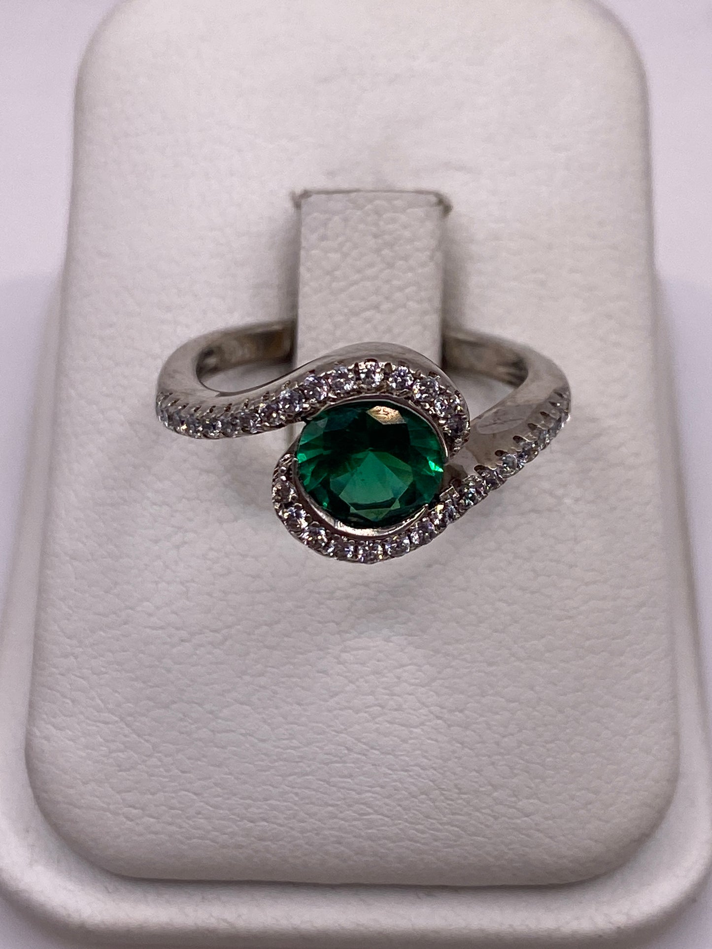 Anillo solitario de plata con circonia verde brillante en espiral, sobre fondo blanco