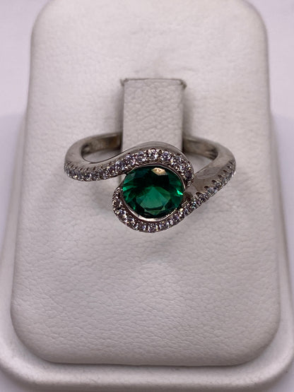 Anillo solitario de plata con circonia verde brillante en espiral, sobre fondo blanco