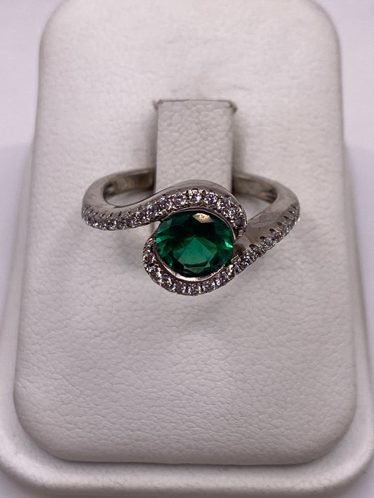 Anillo solitario de plata con circonia verde brillante en espiral, sobre fondo blanco
