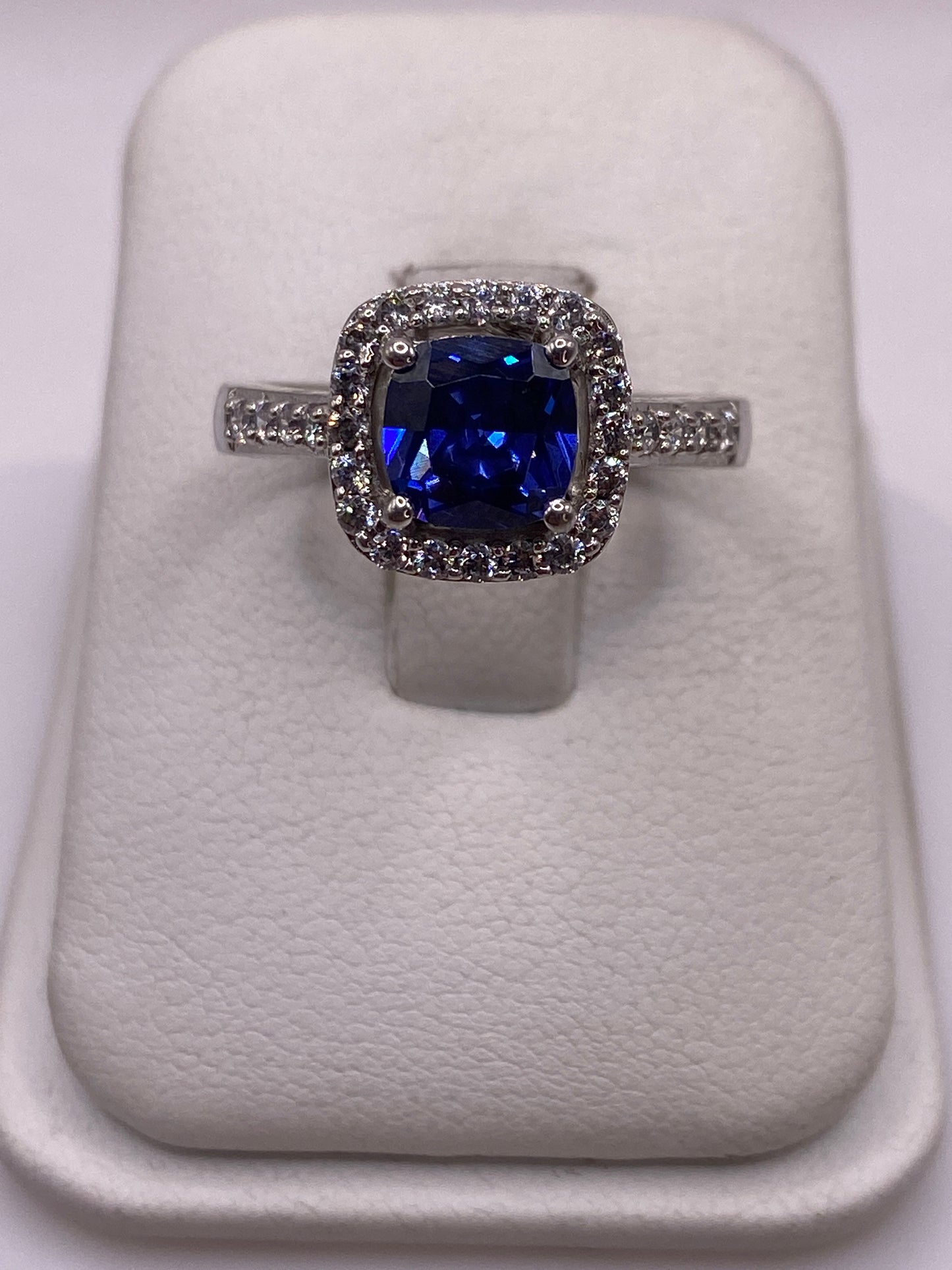 Anillo solitario de plata con circonia azul brillante sobre cojín blanco, vista frontal
