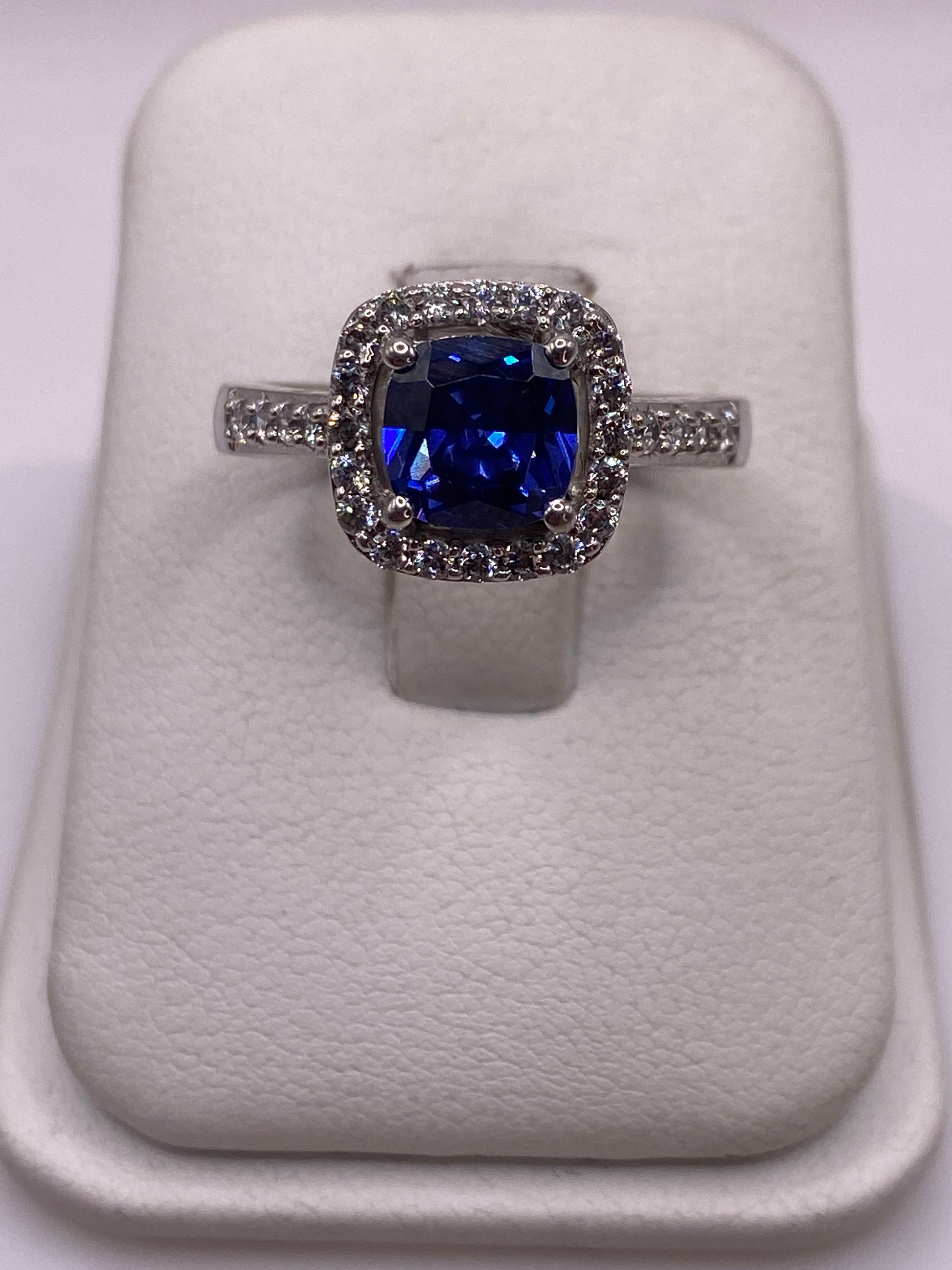 Anillo solitario de plata con circonia azul brillante sobre cojín blanco, vista frontal