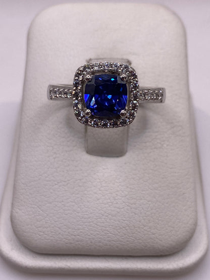 Anillo solitario de plata con circonia azul brillante sobre cojín blanco, vista frontal