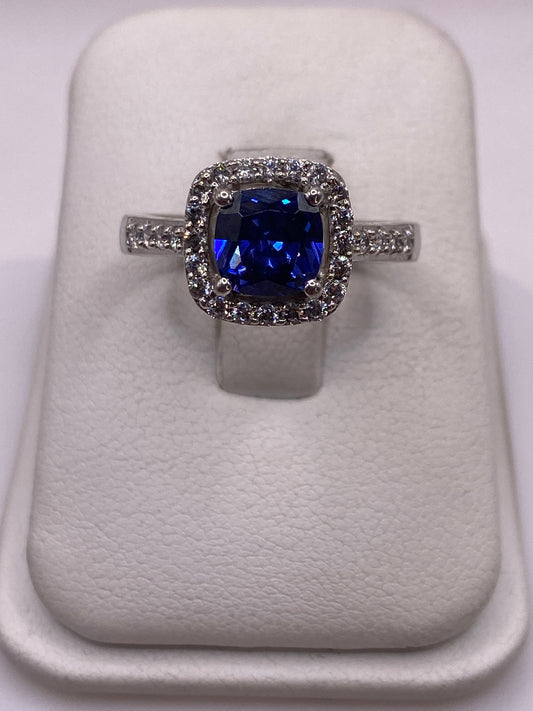 Anillo solitario de plata con circonia azul brillante sobre cojín blanco, vista frontal