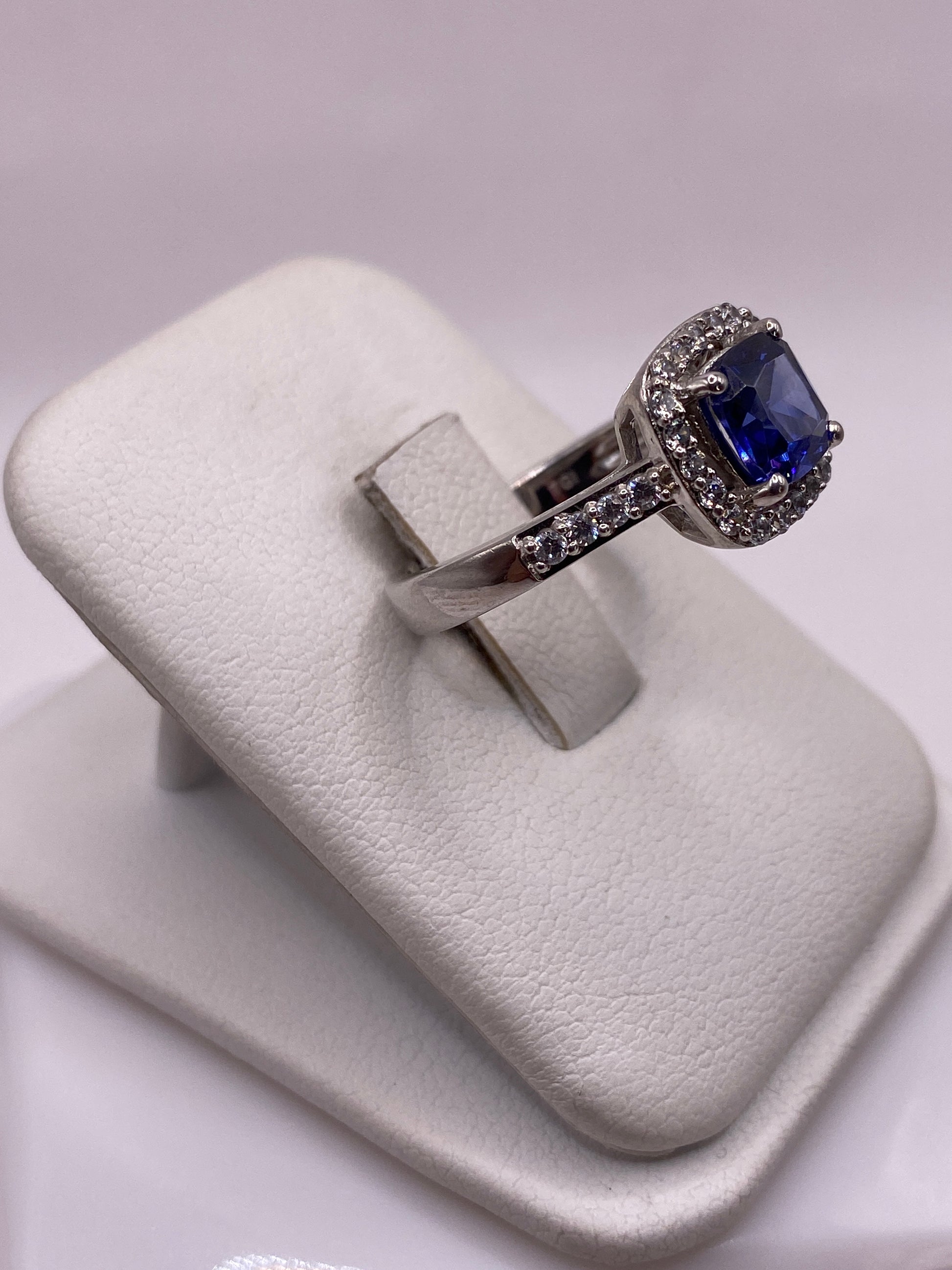 Anillo circonia azul en mano de mujer con maquillaje rosa, mostrando brillo y fuego