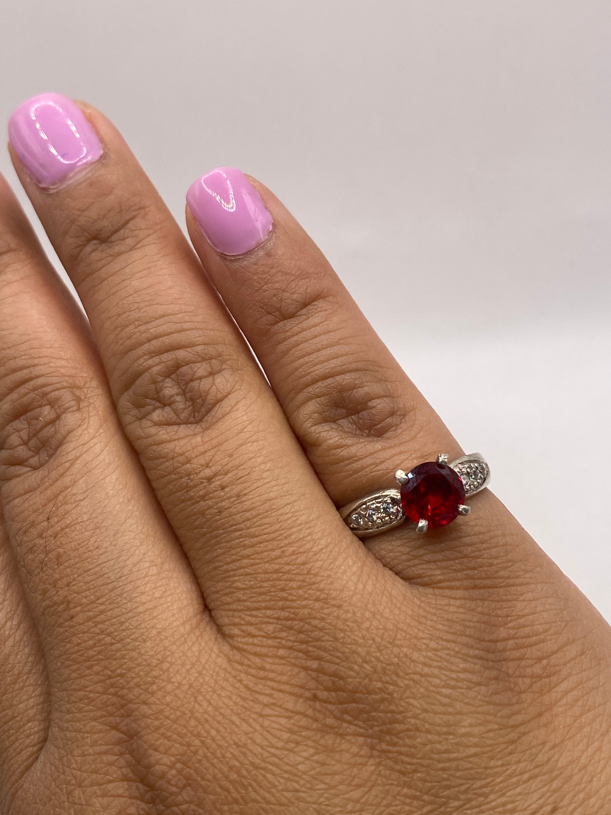 Anillo de plata solitario rojo puesto en dedo con manicura rosa