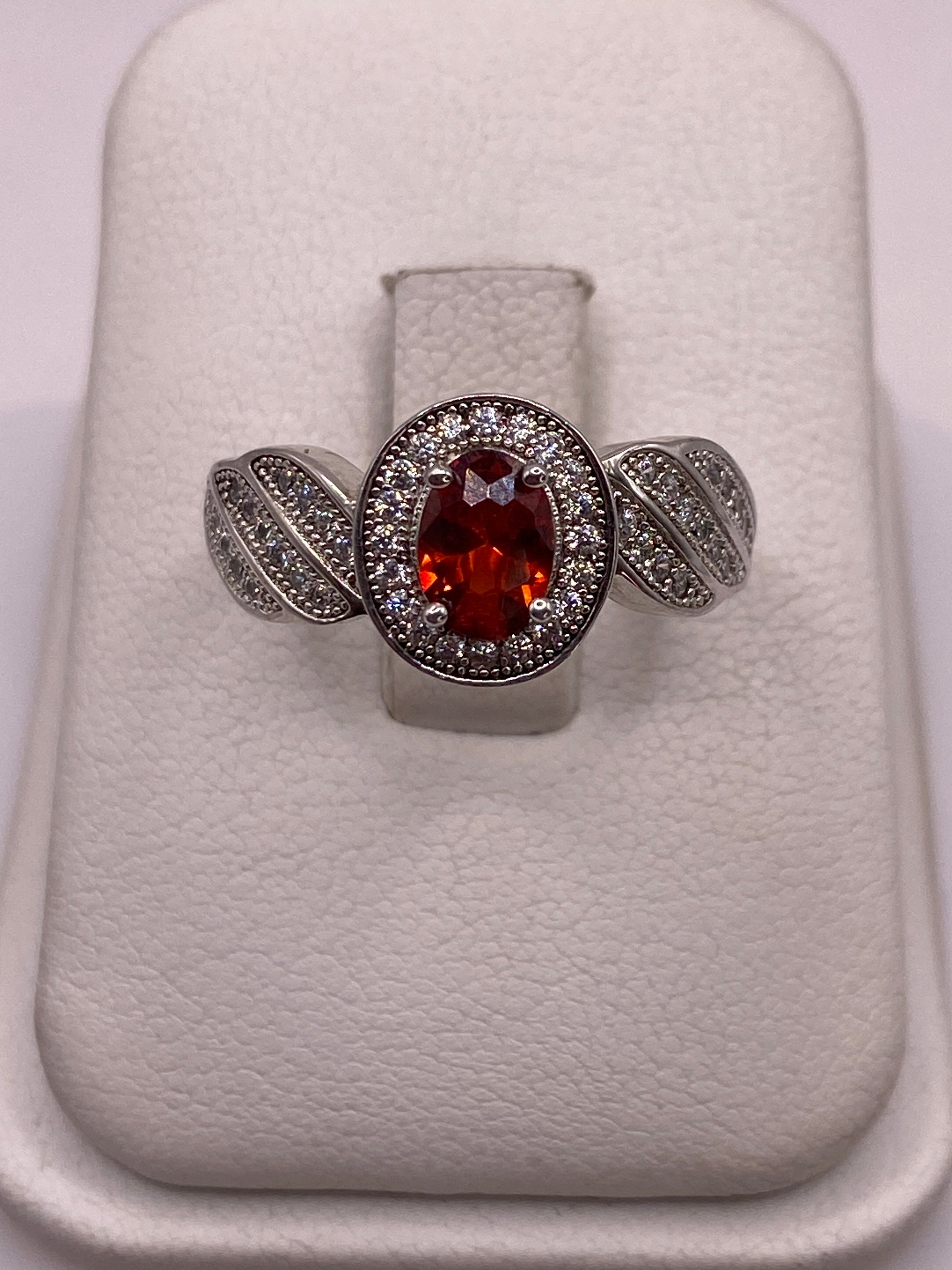 Anillo de plata solitario con circonia naranja facetada y alas decoradas, vista frontal en estuche