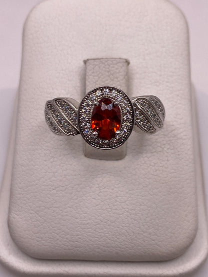 Anillo de plata solitario con circonia naranja facetada y alas decoradas, vista frontal en estuche