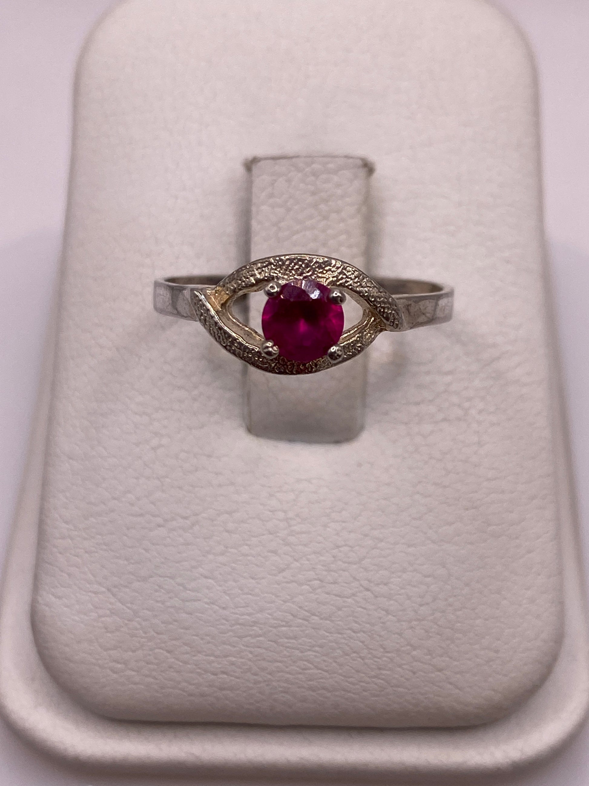 Anillo solitario de plata con circonia roja brillante en posición frontal sobre almohadilla blanca