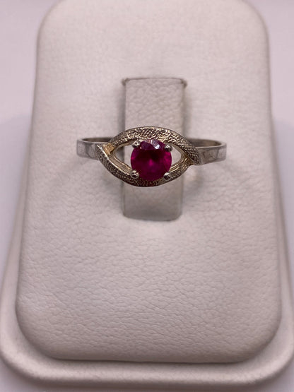 Anillo solitario de plata con circonia roja brillante en posición frontal sobre almohadilla blanca