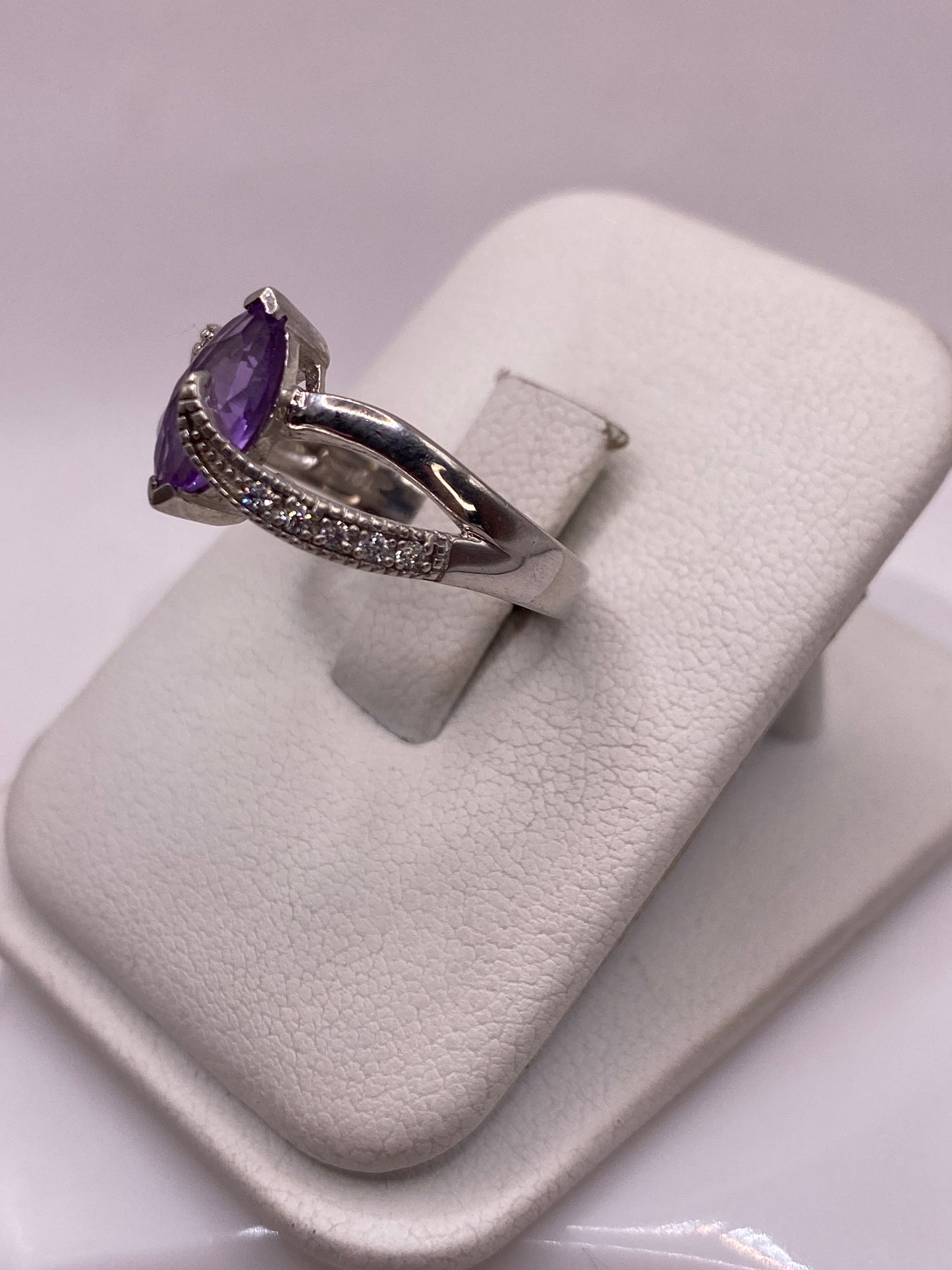 Vista frontal del anillo solitario morado en mano de mujer con esmalte rosa