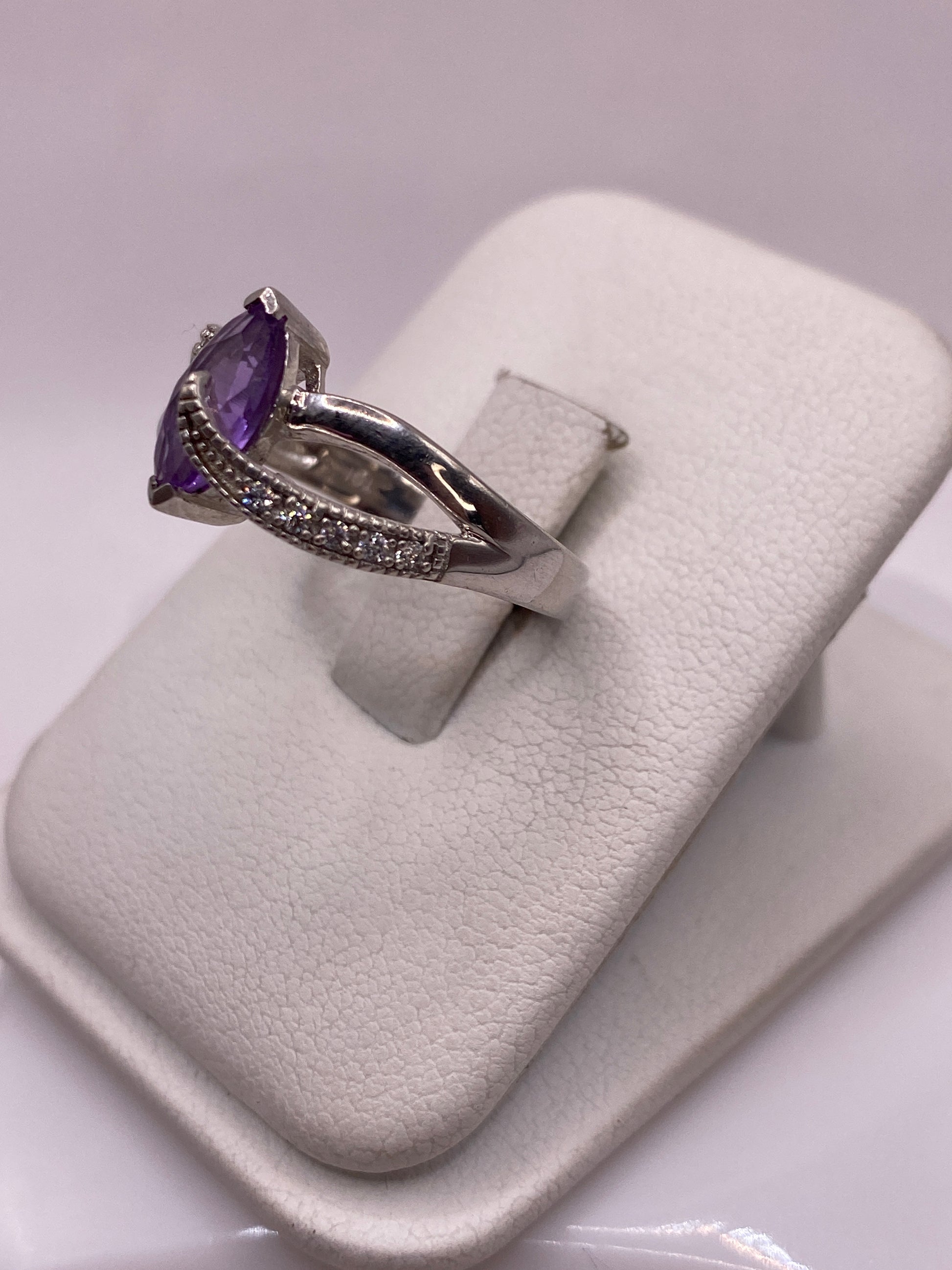 Vista frontal del anillo solitario morado en mano de mujer con esmalte rosa