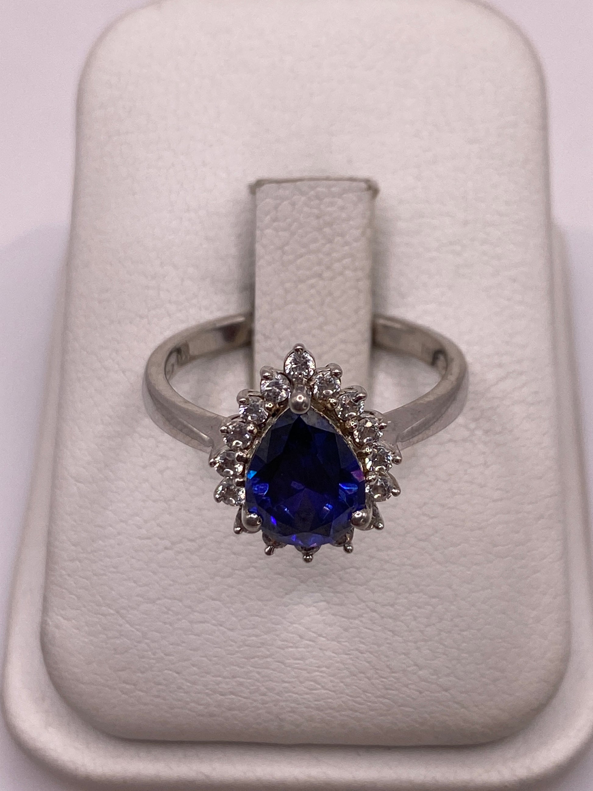 Anillo de plata solitario con circonia morada facetada y halo envolvente, sobre anillo de exhibición blanco
