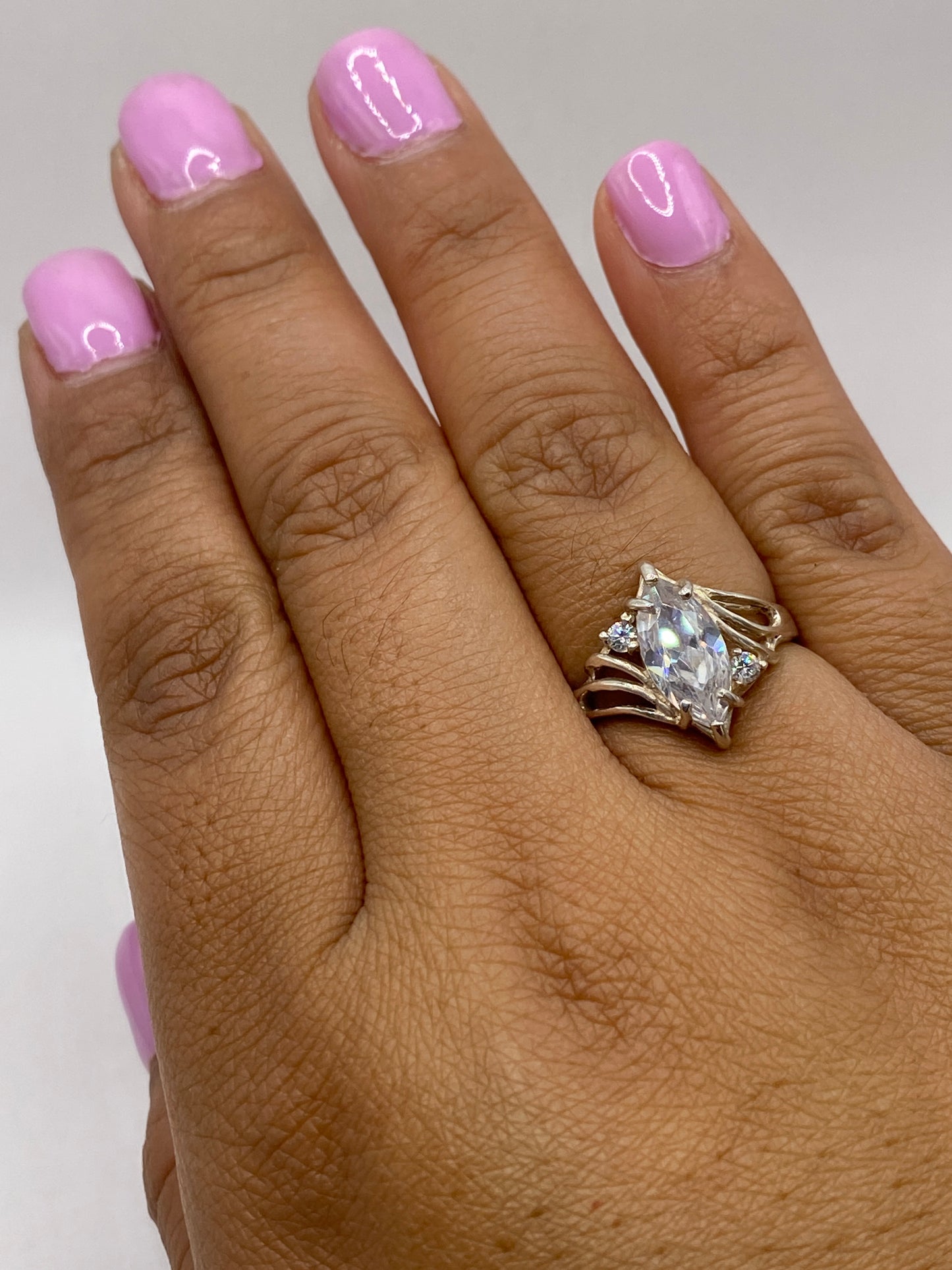 Anillo solitario en dedo de mujer con uñas rosadas, mostrando el brillo natural