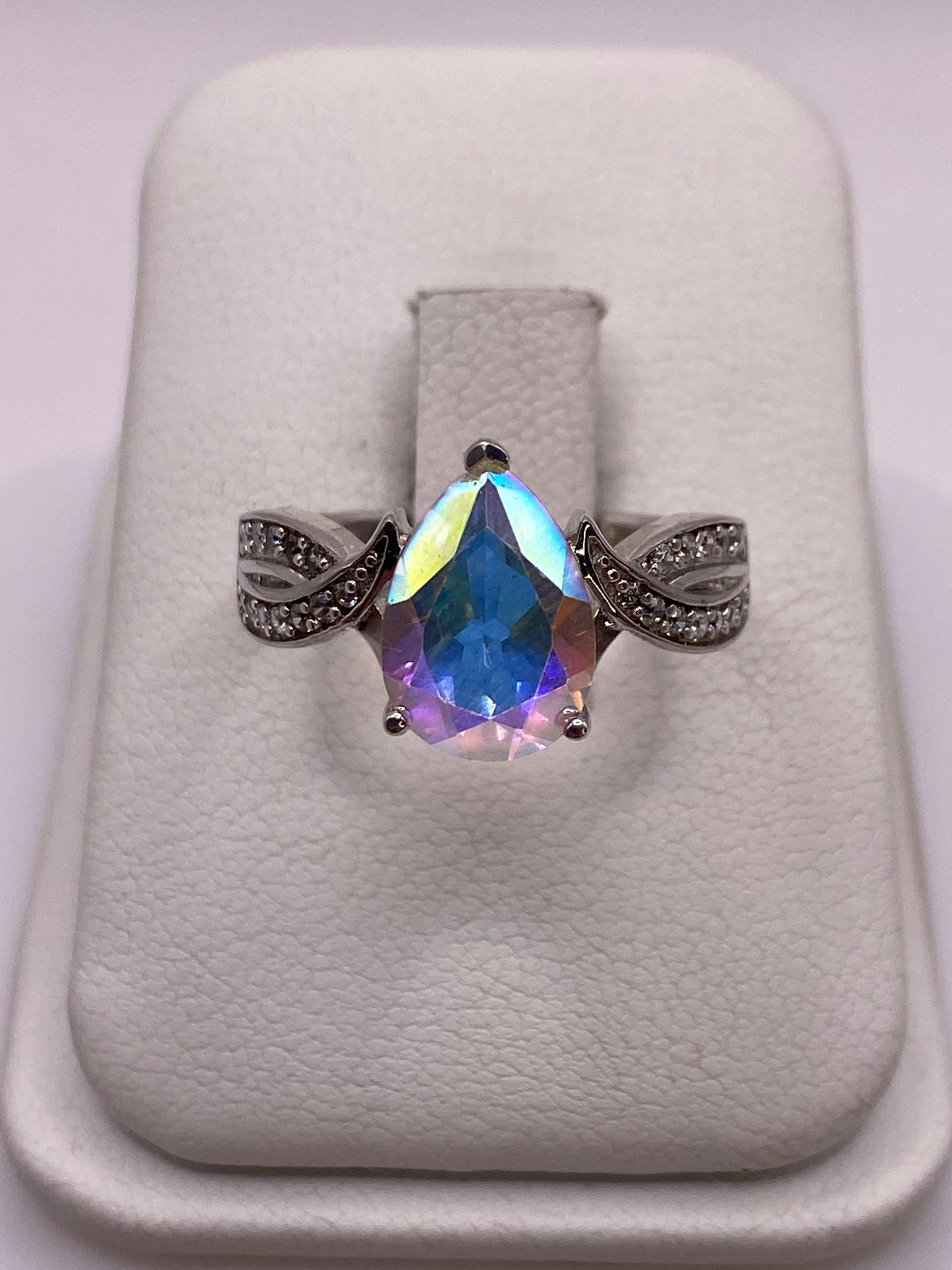 Anillo de plata con gota de circonia arcoíris y alas torneadas, vista frontal sobre soporte blanco