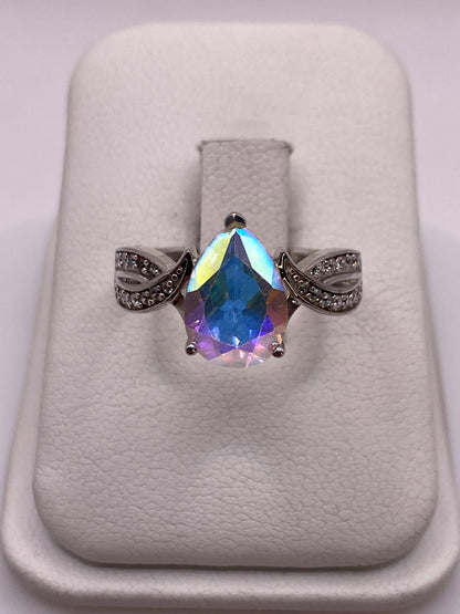 Anillo de plata con gota de circonia arcoíris y alas torneadas, vista frontal sobre soporte blanco
