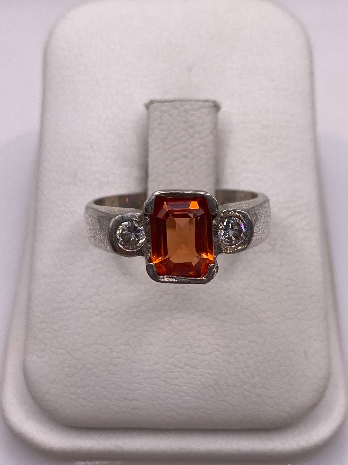 Anillo de plata solitario con circonia naranja brillante sobre dedo con esmalte rosa