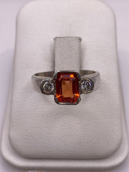 Anillo de plata solitario con circonia naranja brillante sobre dedo con esmalte rosa