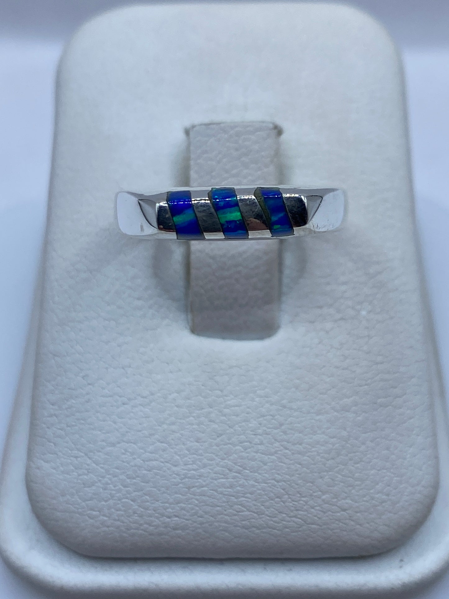 Anillo de plata con ópalo de fuego azul engastado, vista frontal sobre exhibidor blanco