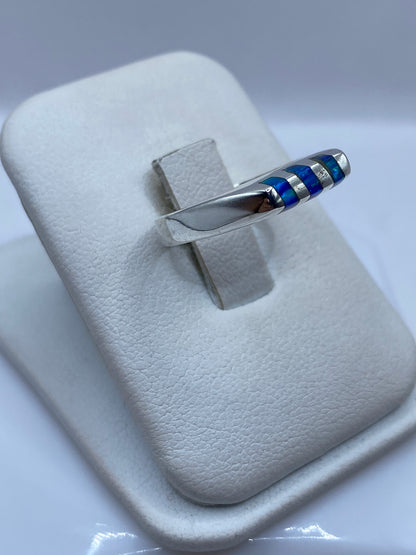 Anillo unisex de plata .925 con ópalo azul en la mano, mostrando el juego de luz