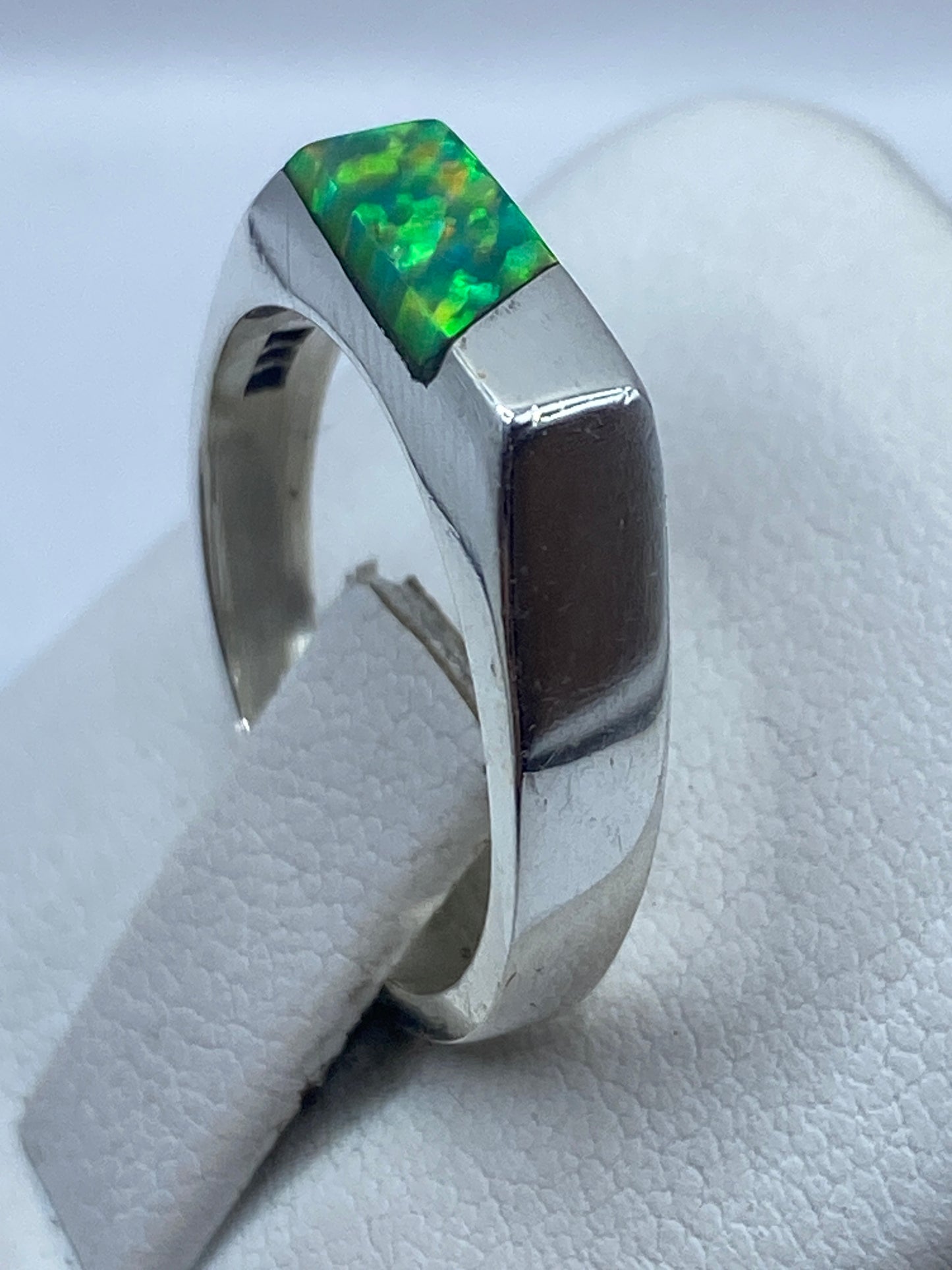 Anillo de plata con ópalo de fuego puesto en dedo, luz natural resaltando los destellos verdes y amarillos