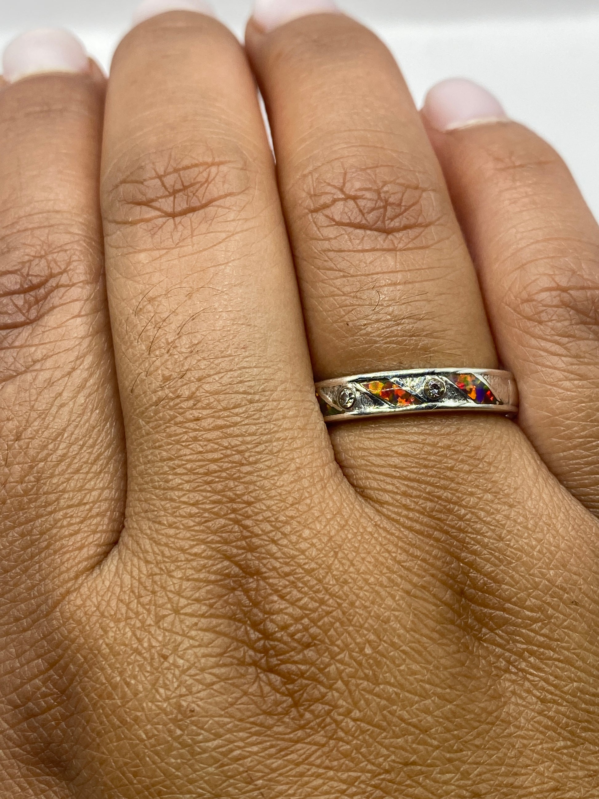 Anillo en dedo de mujer con ópalo de fuego capturando luz natural, colores vivos