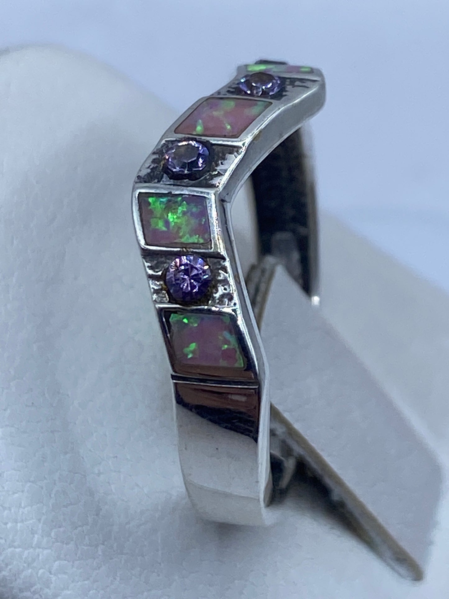 Detalle lateral del anillo en la mano, ópalo de fuego brillando con tonos violeta y rosa
