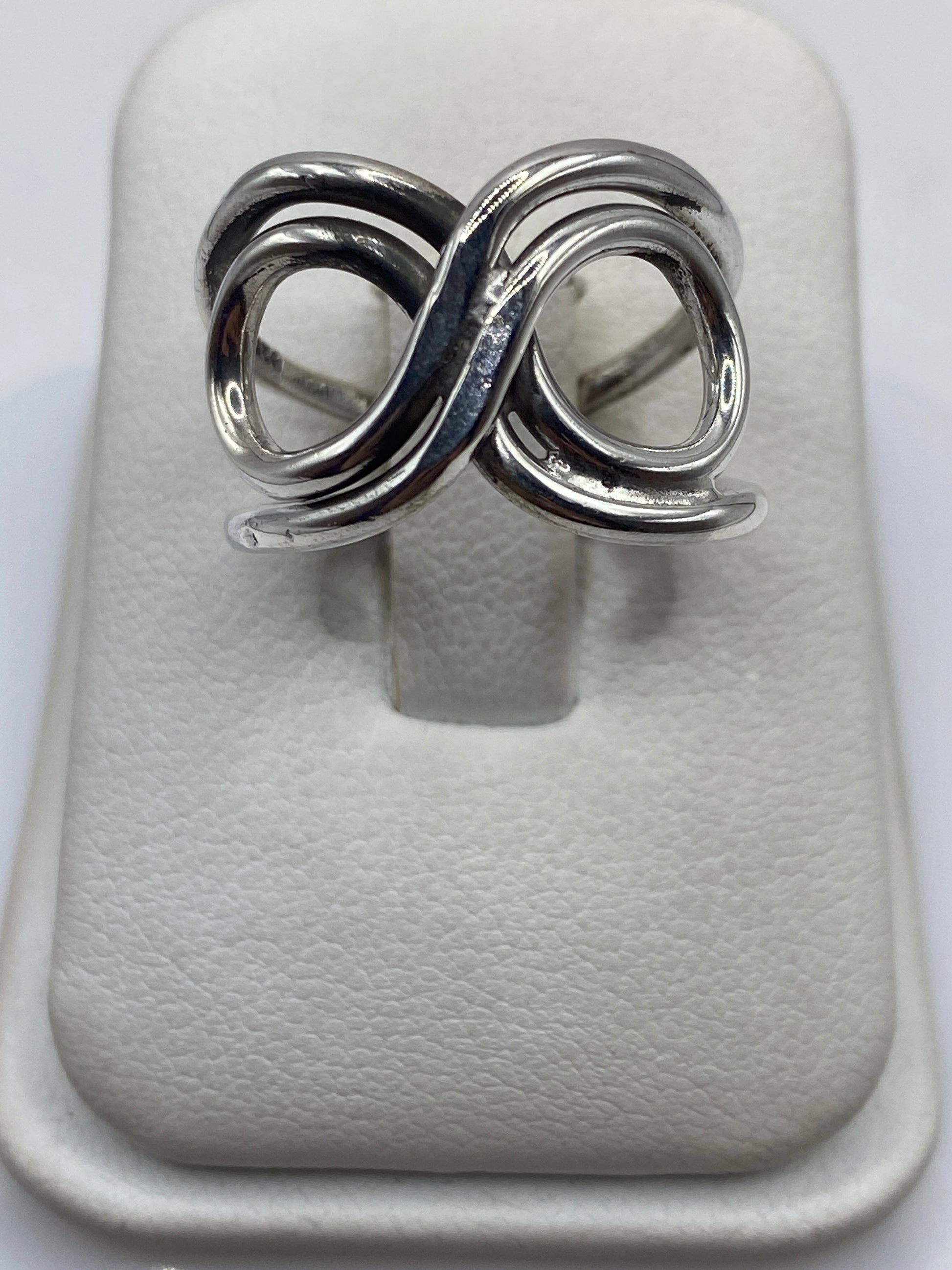 Anillo de plata con doble bucle geométrico entrelazado en la mano de una mujer