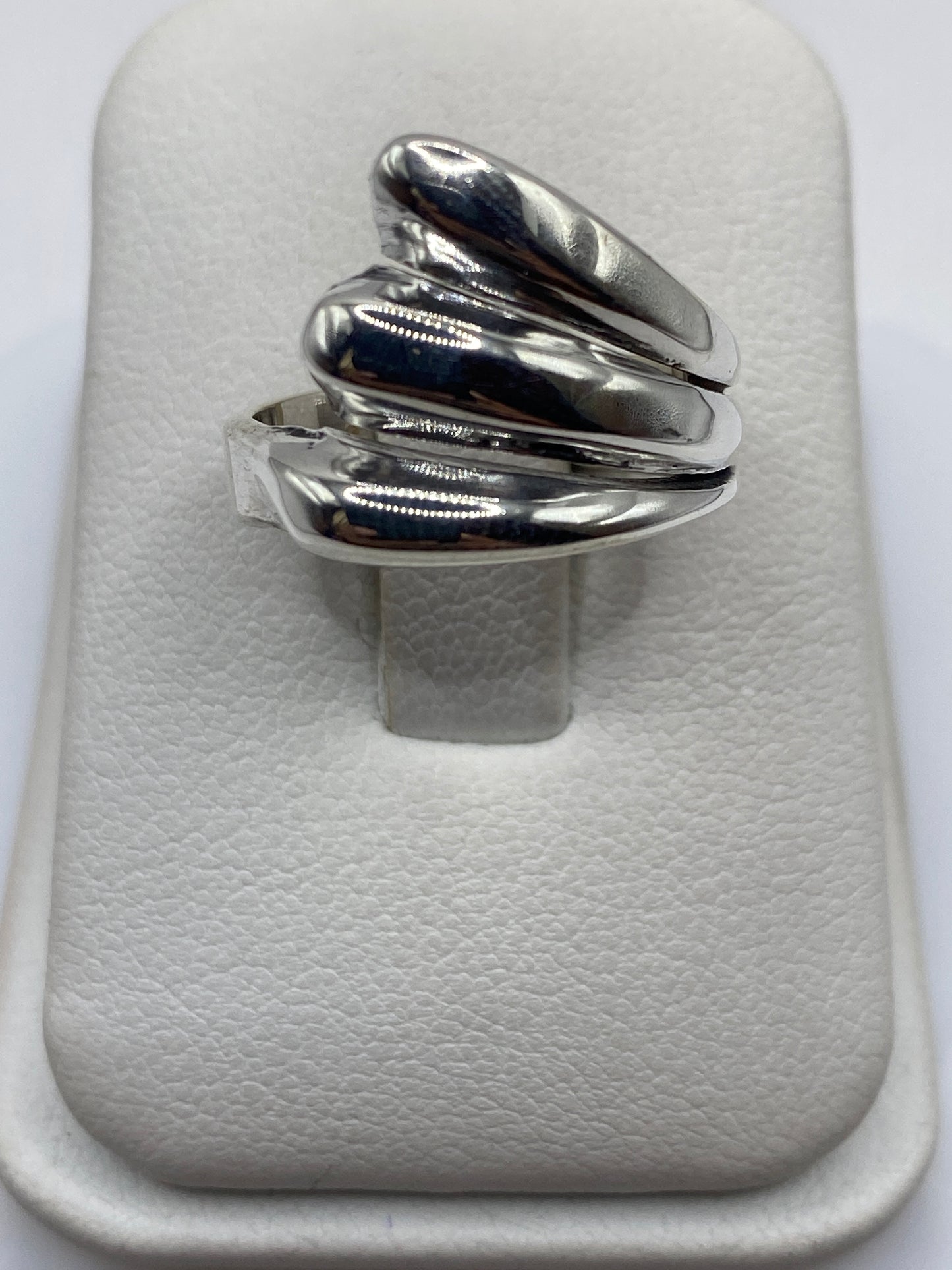 Anillo de plata con pétalos superpuestos en cascada, visto desde arriba sobre fondo blanco