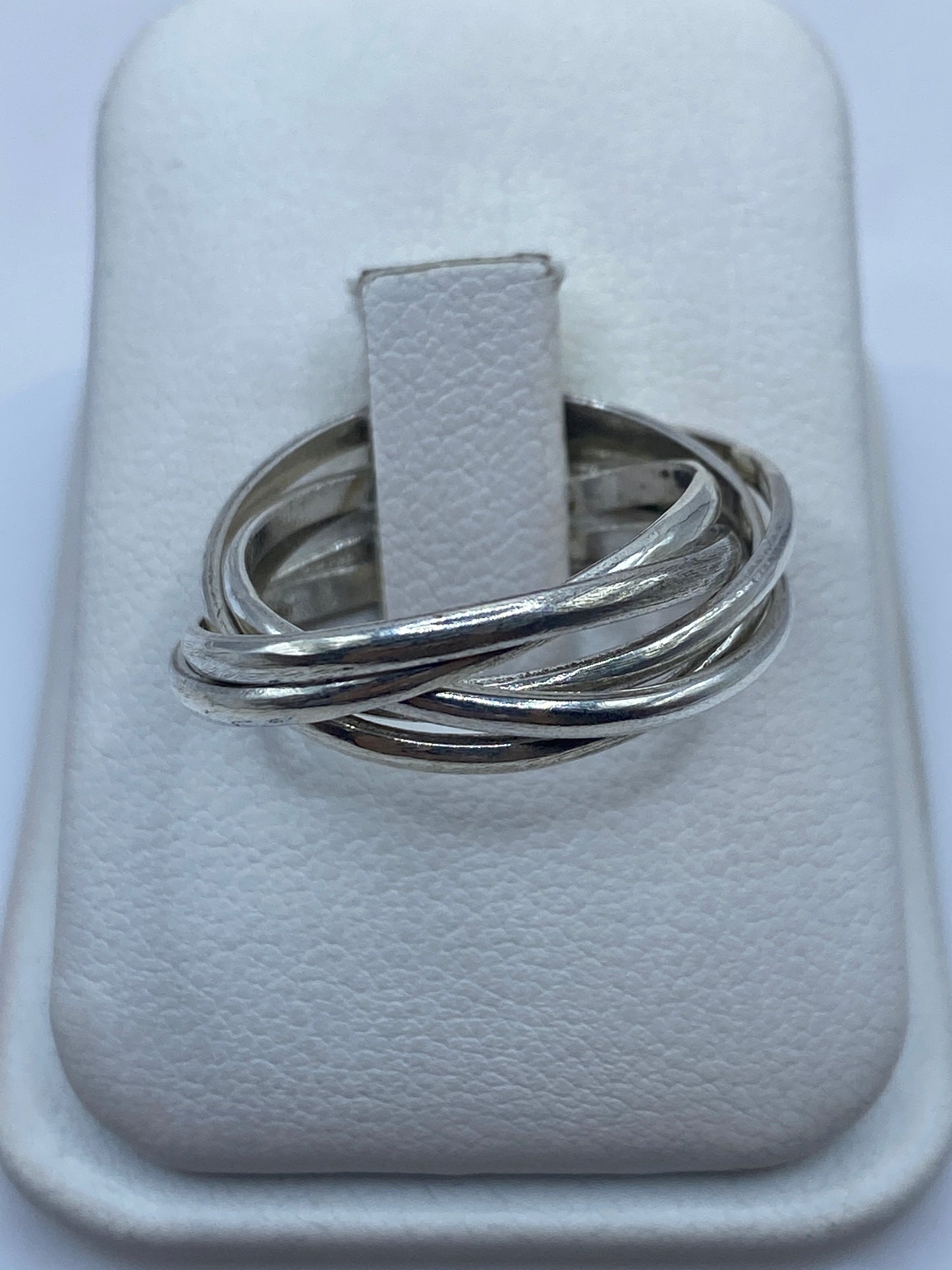 Anillo de plata con tres bandas entrecruzadas pulidas, vista frontal en joyero blanco