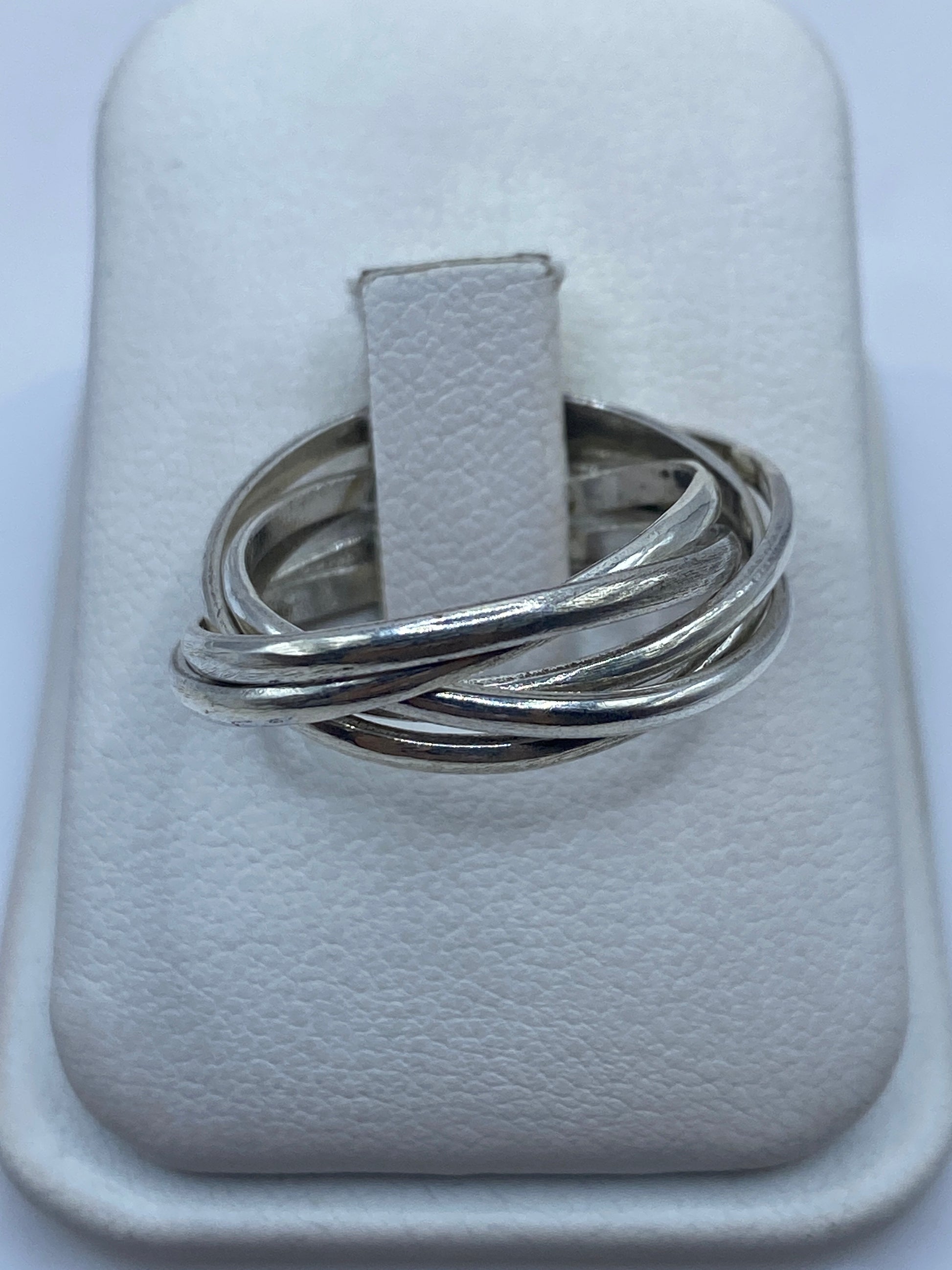 Anillo de plata con tres bandas entrecruzadas pulidas, vista frontal en joyero blanco